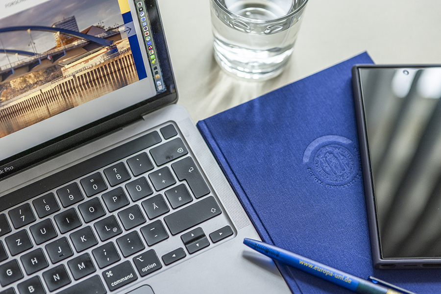 Bild des Laptops, Stift, Wasserglas, Notizbuch und Handy, Ausblick von oben